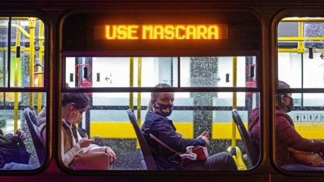 Pessoas de máscara em ônibus onde um letreiro luminoso diz "use máscara"